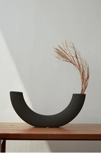 Minimalistische mattschwarze U-Vase aus Keramik mit Trockenblumen auf einem Holztisch
