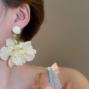 Detail showing oversized white fabric flower earring with beaded tassel on a model