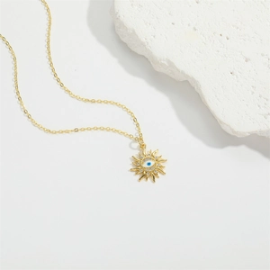 Golden sunburst evil eye pendant necklace with white zircon on white stone background