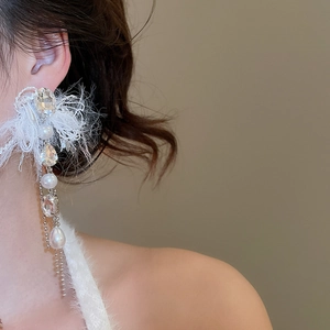 Close-up of elegant long earrings with white feathers, crystals and pearls on model