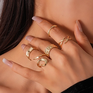 Detail of five-piece gold geometric ring set with textured and cross designs on a model