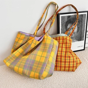 Detailed view of yellow and orange plaid canvas tote bags on a textured rug