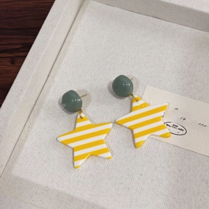 Close-up of star-shaped striped resin earrings with green beads on a white jewelry tray