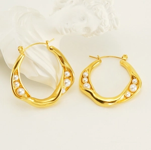 Detailed view of gold wave hoop earrings with graduated pearls on a marble statue