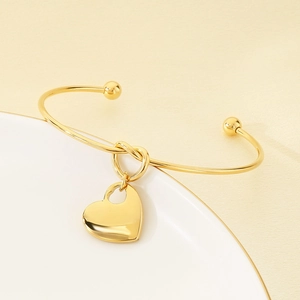 Close-up of golden heart knot open bangle featuring double ball ends on a white ceramic plate