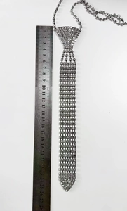 Macro shot of silver rhinestone tie necklace next to a ruler showing its 25cm length