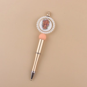 Detail of champagne gold beaded pen with pink sphere and floral pearl-bordered top