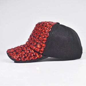 Dettaglio cappello nero con strass ovali rossi sulla visiera e parte anteriore