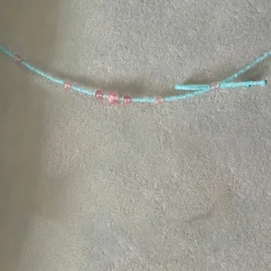 Gros plan du collier en perles bleu ciel avec cristaux roses et détail de nœud fait main