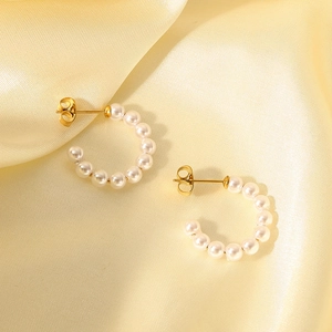 Detail of C-shaped gold earrings with small white pearls on elegant silk fabric