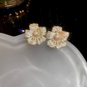 Detailed close-up of golden flower stud earrings with shimmering white zircons