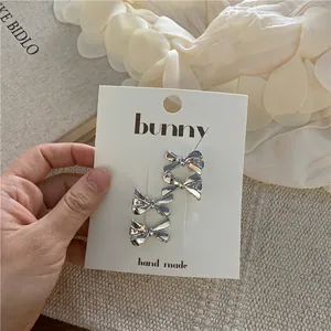 Close-up of four silver bow-shaped hair clips on a white card with a polished mirror finish
