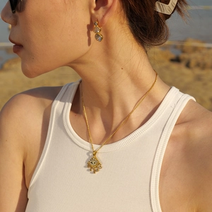 Mannequin portant un collier œil grec doré et boucles d'oreilles zircon sur la plage