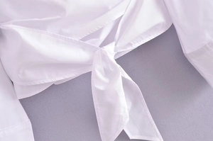 Détail du nœud à la taille et de la texture du coton sur cette chemise blanche