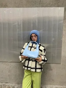 Detail of light blue patent leather crescent bag paired with a plaid jacket and knit hat