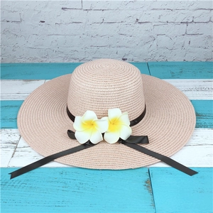 Detail of a straw sun hat with wide brim, black ribbon, and white frangipani flowers