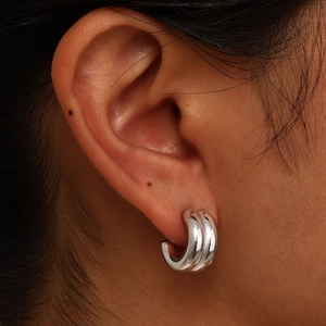 Detail of silver double-layered C-shaped stainless steel hoop earrings on a model