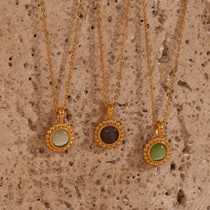 Close-up of triple gold sun pendants with green and purple cat eye stones on stone surface