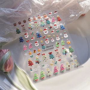 Vue macro de stickers ongles 3D de Noël avec Père Noël, sapins et flocons dorés en relief