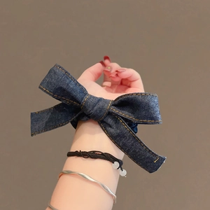 Élastique à cheveux en denim avec nœud et coutures jaunes, porté au poignet sur fond marron