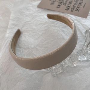 Detailed view of beige glossy PU leather headband with interior fabric lining on glass stand