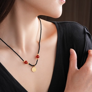 Close-up of golden Fu pendant with red beads on a black cord necklace for women