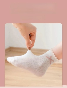 Close-up of white mesh cotton baby socks showing stretchable fabric and pink bow detail