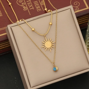 Detail of gold double-layer necklace with sun and blue evil eye charms on jewelry box