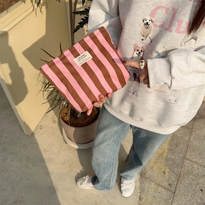 Striped canvas cosmetic bag in pink and brown held by a model for size perspective