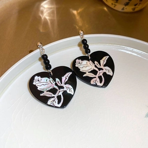 Detail of heart-shaped black drop earrings with pearl-like rose inlay on a ceramic plate