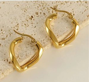 Detail view of irregular twisted gold earrings on a minimalist stone surface