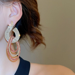 Close-up of geometric gold drop earrings with pink and white rhinestones on a model