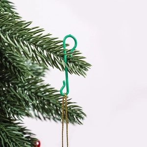 Close-up of a green plastic S-shaped hook hanging a gold chain on a pine branch