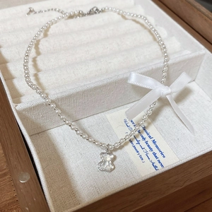 Close-up of pearl necklace with a bear pendant and a white ribbon bow in a jewelry box