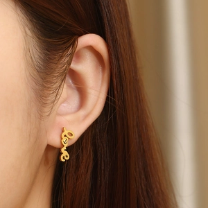 Close-up of golden LOVE letter earrings with tiny heart detail worn by a model