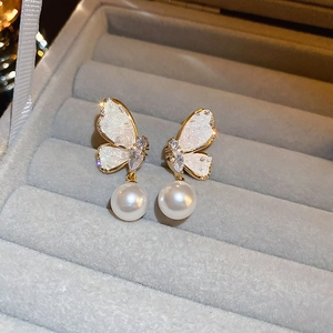 Macro view of butterfly earrings with crystal wings and white pearl drop on velvet