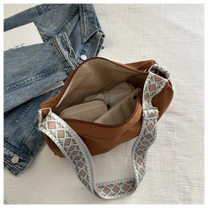 Macro shot of spacious nylon shoulder bag with ethnic pattern strap and interior items