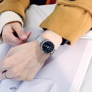 Close-up of silver mesh watch with black dial worn on wrist over orange fabric