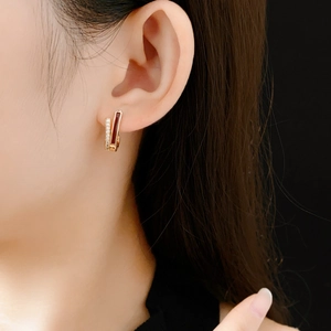 Gros plan sur boucle d'oreille dorée courbée avec incrustation brun rouge et zircons brillants
