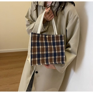 Brown and beige plaid fabric handbag with woven handle and snap closure shown on a model