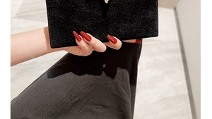 Close-up of black velvet envelope clutch bag held by model with red manicured nails