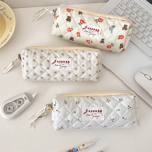 Lot de trois trousses matelassées avec motifs fleurs et ours sur un bureau blanc