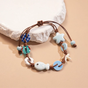 Detail of hand-woven bracelet with ceramic starfish and fish charms on textured stone
