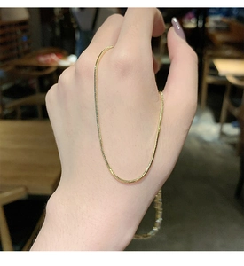 Detail of a minimalist gold snake chain necklace with smooth polished metallic finish