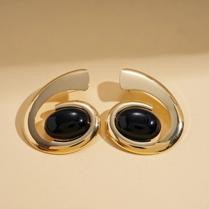 Detailed view of gold spiral earrings with inlaid large black oval gemstones on beige background