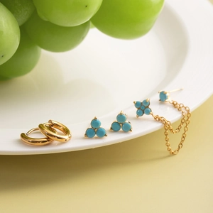 Dreiteiliges Set aus Türkis- und Gold-Edelstahl-Ohrringen auf einer weißen Keramikplatte
