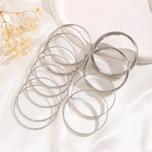 Close-up of 12 vintage silver alloy bangles with textured patterns on white silk cloth