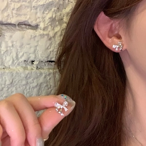 Elegant silver bow stud earrings with zircon crystals shown on ear and held in hand