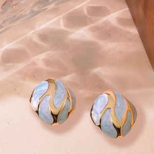 Detailed shot of vintage gold earrings with light blue marbled enamel on a textured surface
