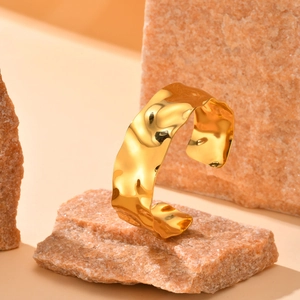 Close-up of golden open bangle with irregular wavy texture on a natural stone background